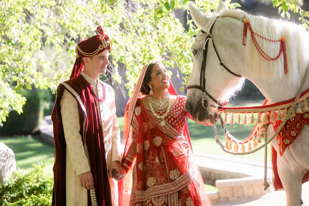 Fusion Couple, traditional bride wearing a red lehenga with intricate gold embroidery, adorned with stunning jewelry,