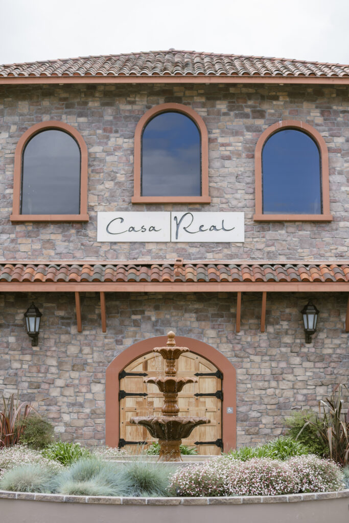 Facade of a stone building with arched windows and a large arched wooden door, a sign reading "Casa Real" is visible.